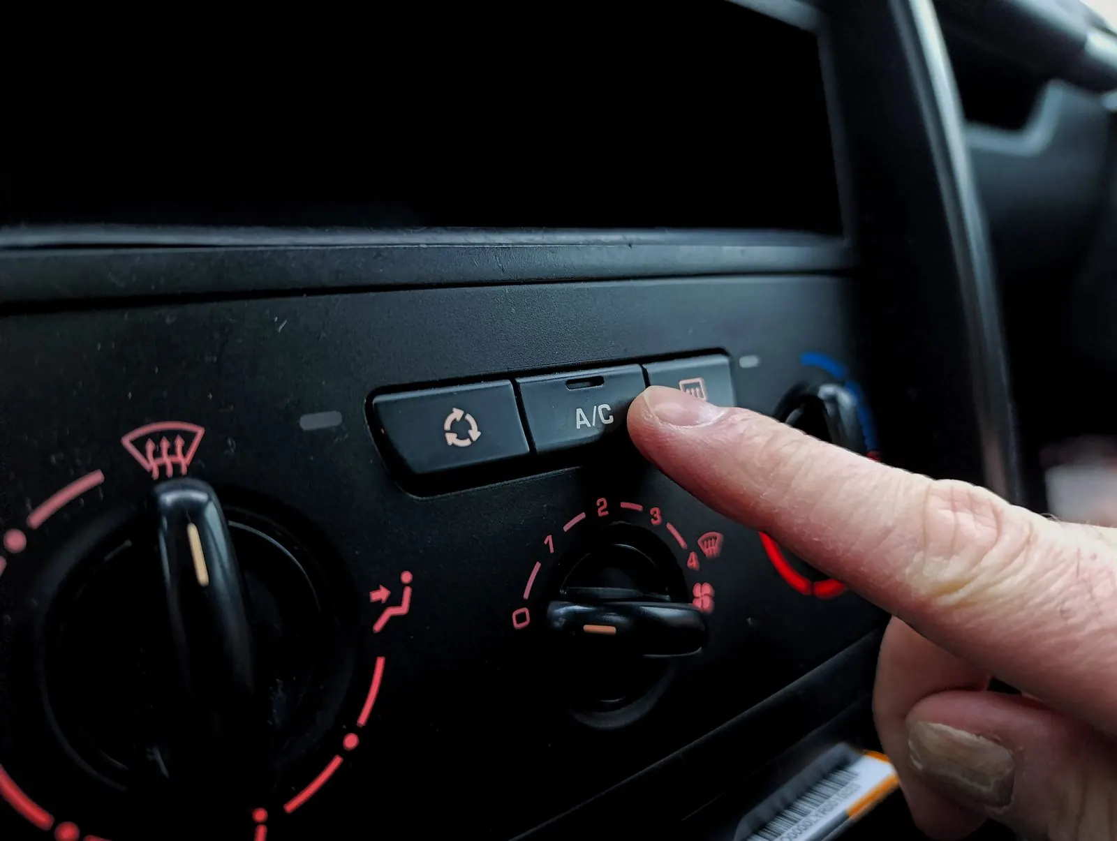 Pressing the A/C button on a car dashboard